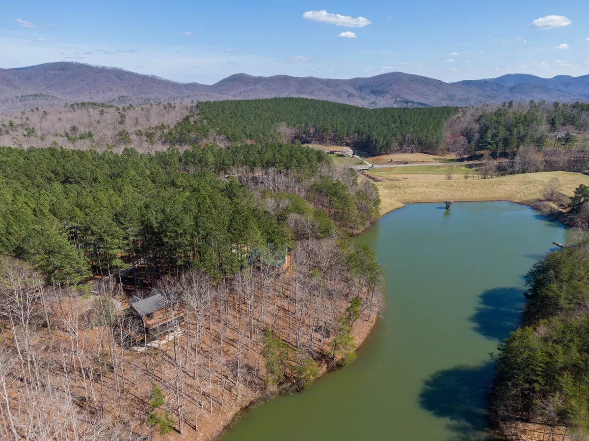 A peaceful, expansive view of a lake surrounded by mountains and dense forest, taken from a vantage point that could represent the view from the loft workspace. The scenery is tranquil and inspiring, with the calm waters reflecting the sky and treetops, providing a strong visual cue for rejuvenation and focus.