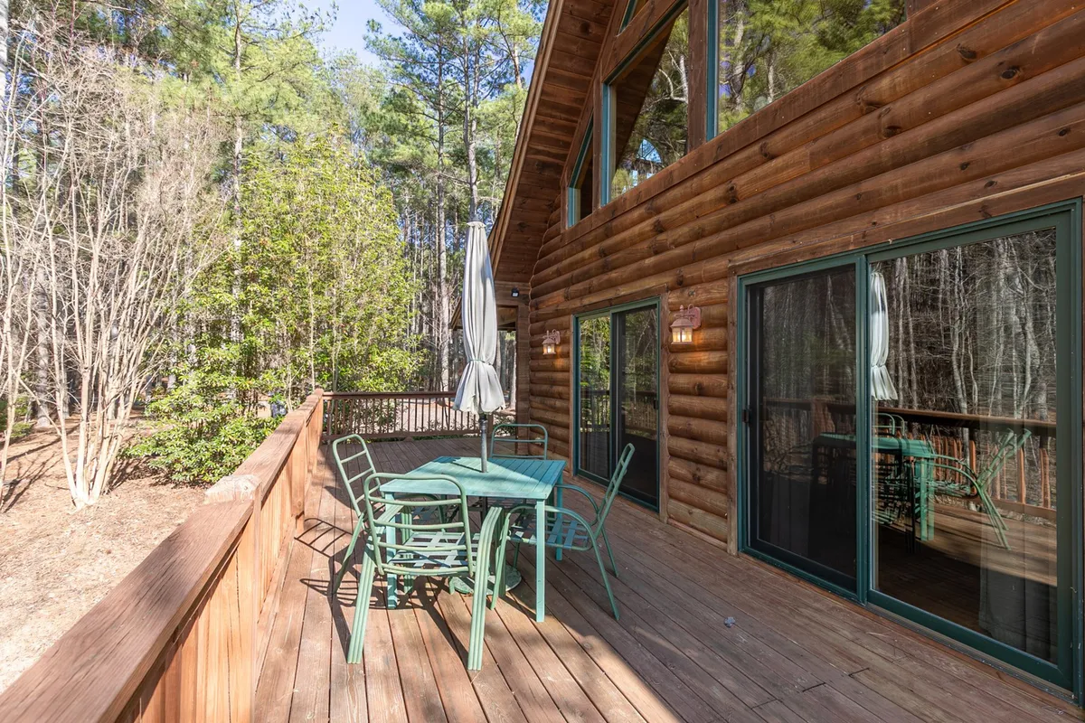 This image showcases a wooden deck with comfortable outdoor seating, surrounded by lush greenery and large windows that reflect the forest. The tranquil setting invites relaxation and offers a seamless transition between indoors and outdoors.