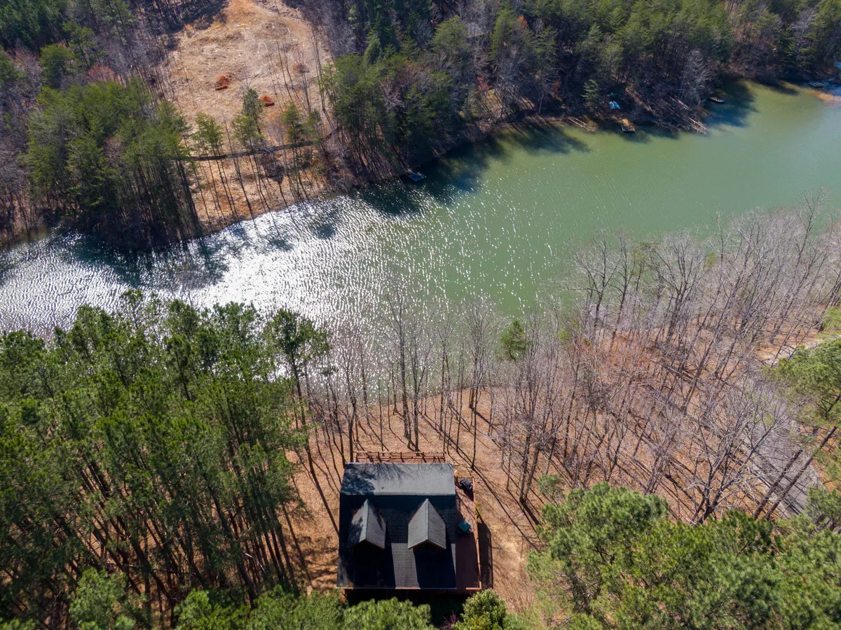 The image features a cozy log cabin nestled among tall trees with sweeping views of tranquil Hidden Lake. The golden hues of sunset reflect off the water, while the spacious deck invites guests to relax and soak in nature's beauty. The peaceful setting is complemented by hints of outdoor activities like a canoe on the shoreline and walking paths leading into the woods.
