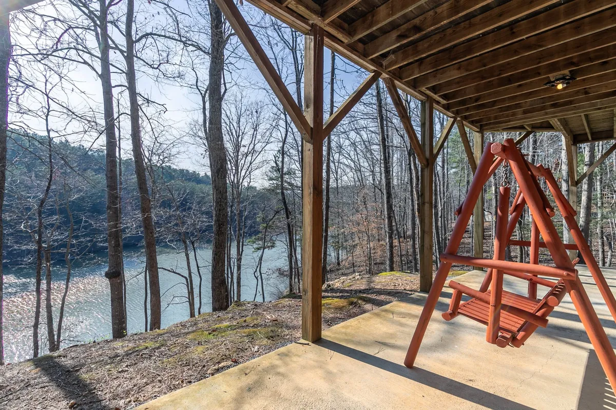 A peaceful lakeside scene featuring a swing facing the calm water, surrounded by trees. The setting invites relaxation, quiet conversation, or simply enjoying nature’s beauty, ideally suited for couples looking for a romantic retreat.