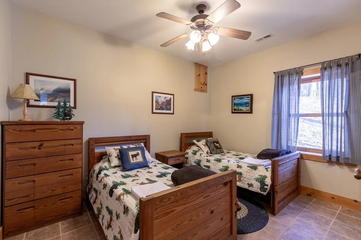 A cheerful twin room featuring two twin beds, a wooden dresser, a window with curtains, and decorative wall art, creating a welcoming space for guests.