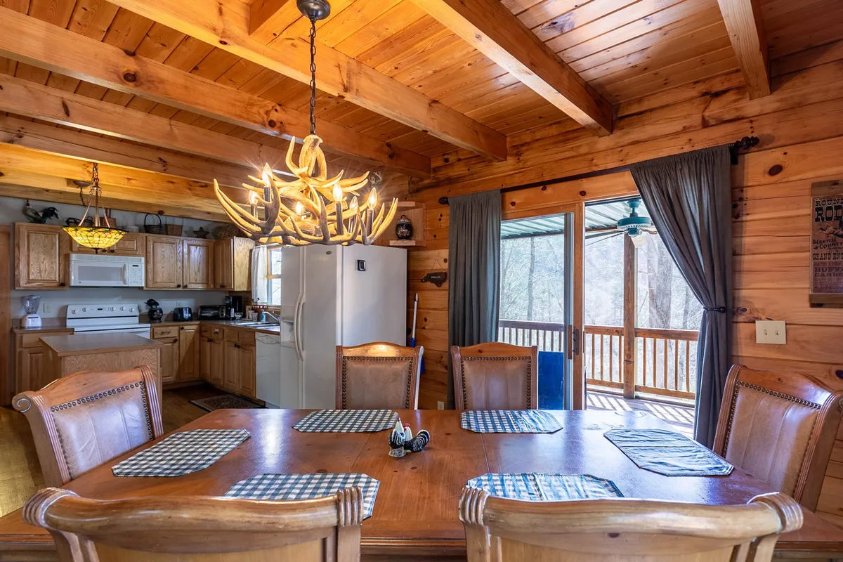 The image features a spacious dining area with a prominent wooden table and elegant chandelier, seamlessly connected to a modern kitchen and a sliding door leading to the outdoor deck. The scene is ideal for illustrating shared meals and easy indoor-outdoor flow.